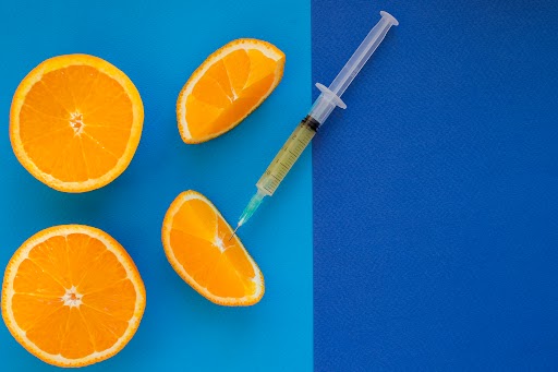 Vitamin C brown ampule with syringe on fresh juicy orange fruit slides